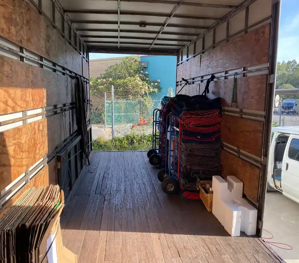 Image-24-scaled | Will Move Removalist Interior of an empty moving truck with wooden side walls; red and gray mats stacked on rolling carts along the right side near the doorway.