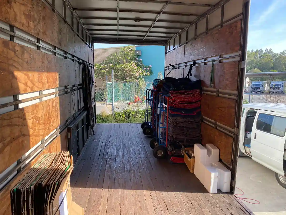 Interior of an empty moving truck with wooden side walls; red and gray mats stacked on rolling carts along the right side near the doorway.