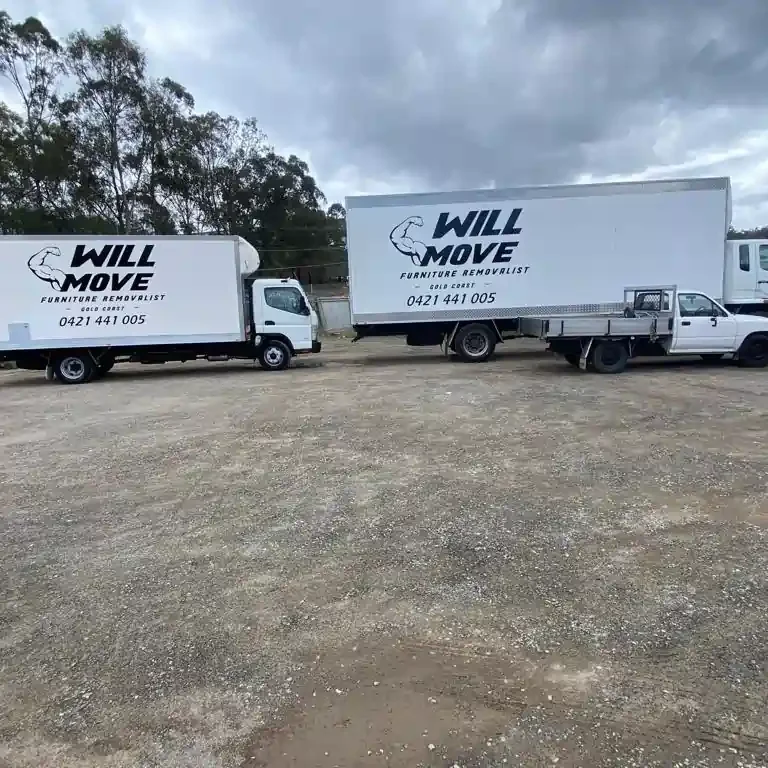 WIll-Move-Van-3 | Will Move Removalist Two white Will Move furniture removal trucks parked on a gravel lot beneath a cloudy sky.